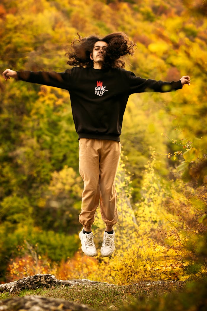 Energetic jump shot of a young man in autumn forest wearing a black sweatshirt and beige pants.