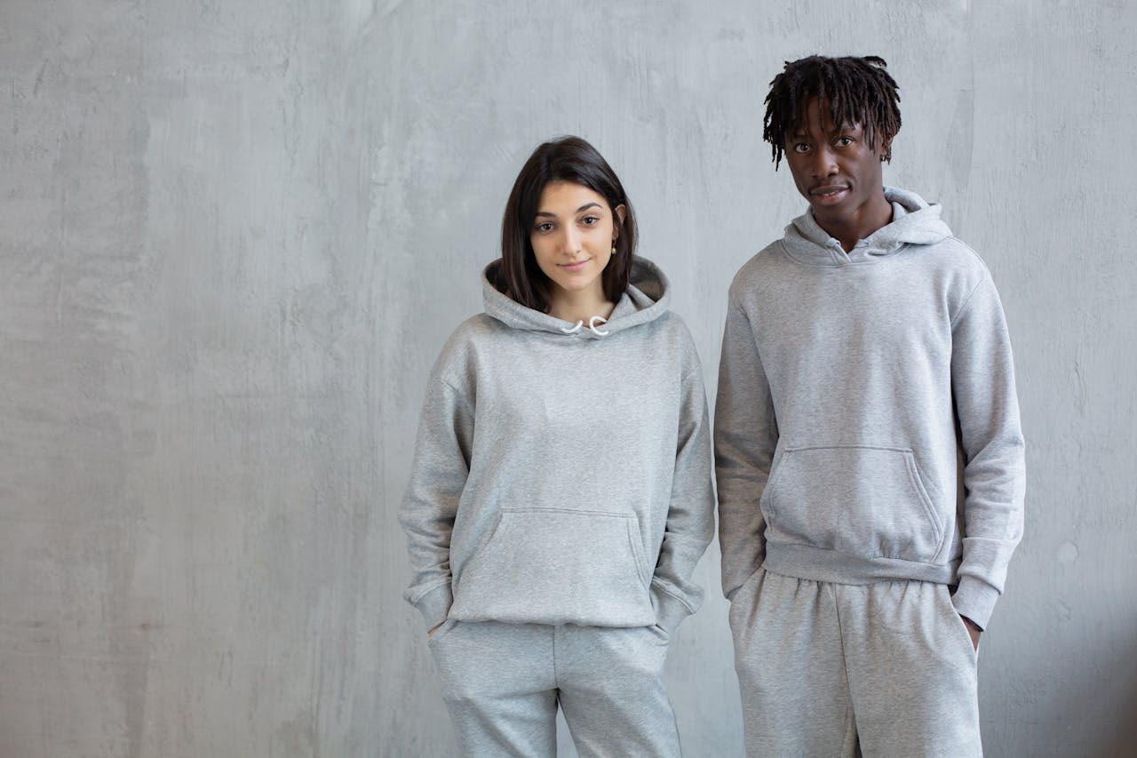 Smiling diverse man and woman wearing similar sports suits standing with hands in pockets and looking at camera
